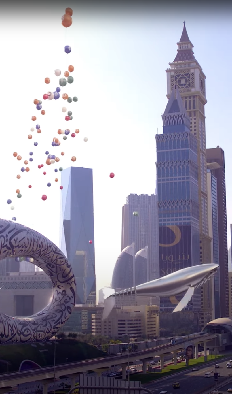 Metal whale beside Museum of the Future with colorful floating coins.