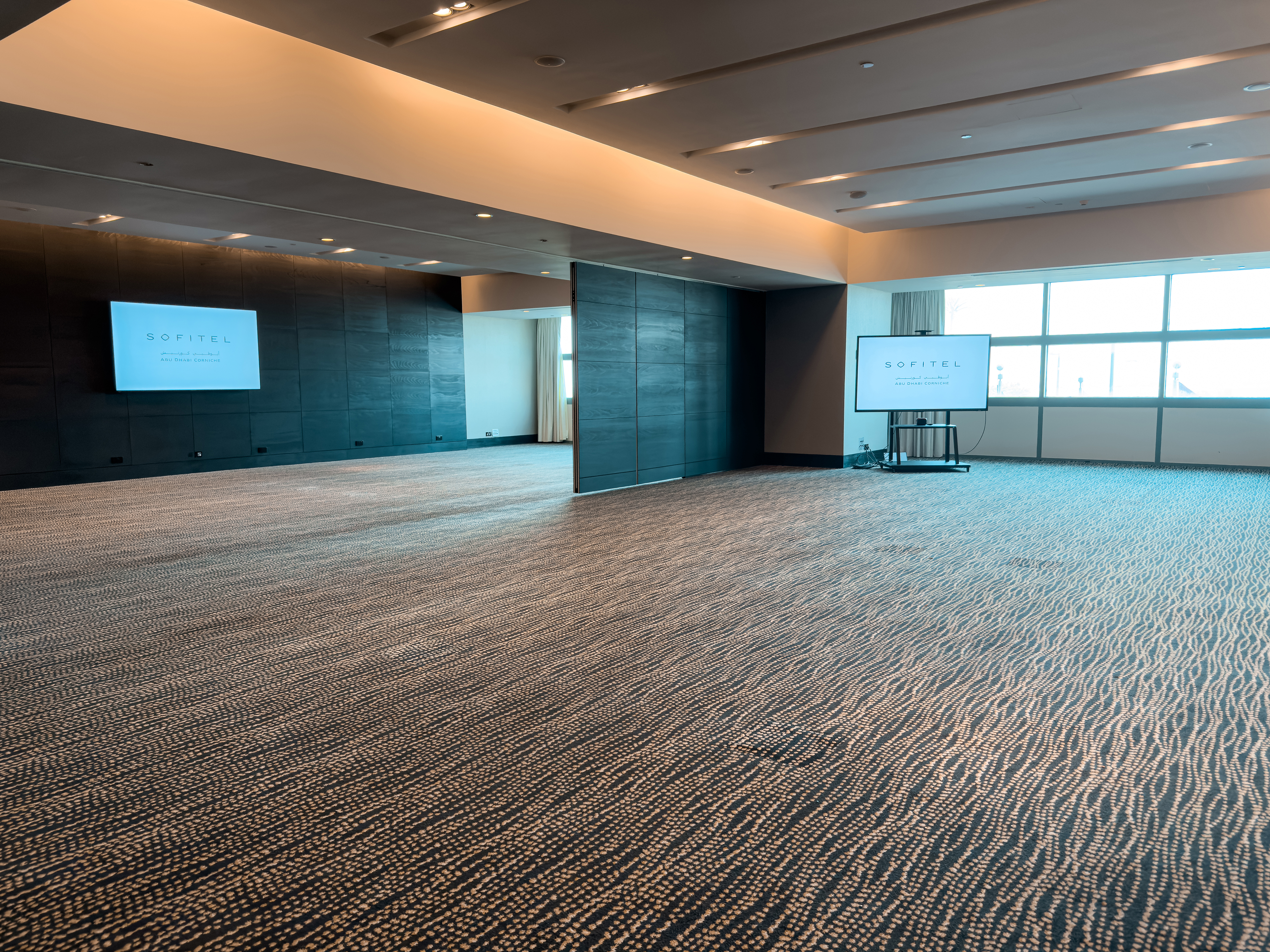 Large meeting hall at Sofitel Abu Dhabi Corniche with presentation screens.